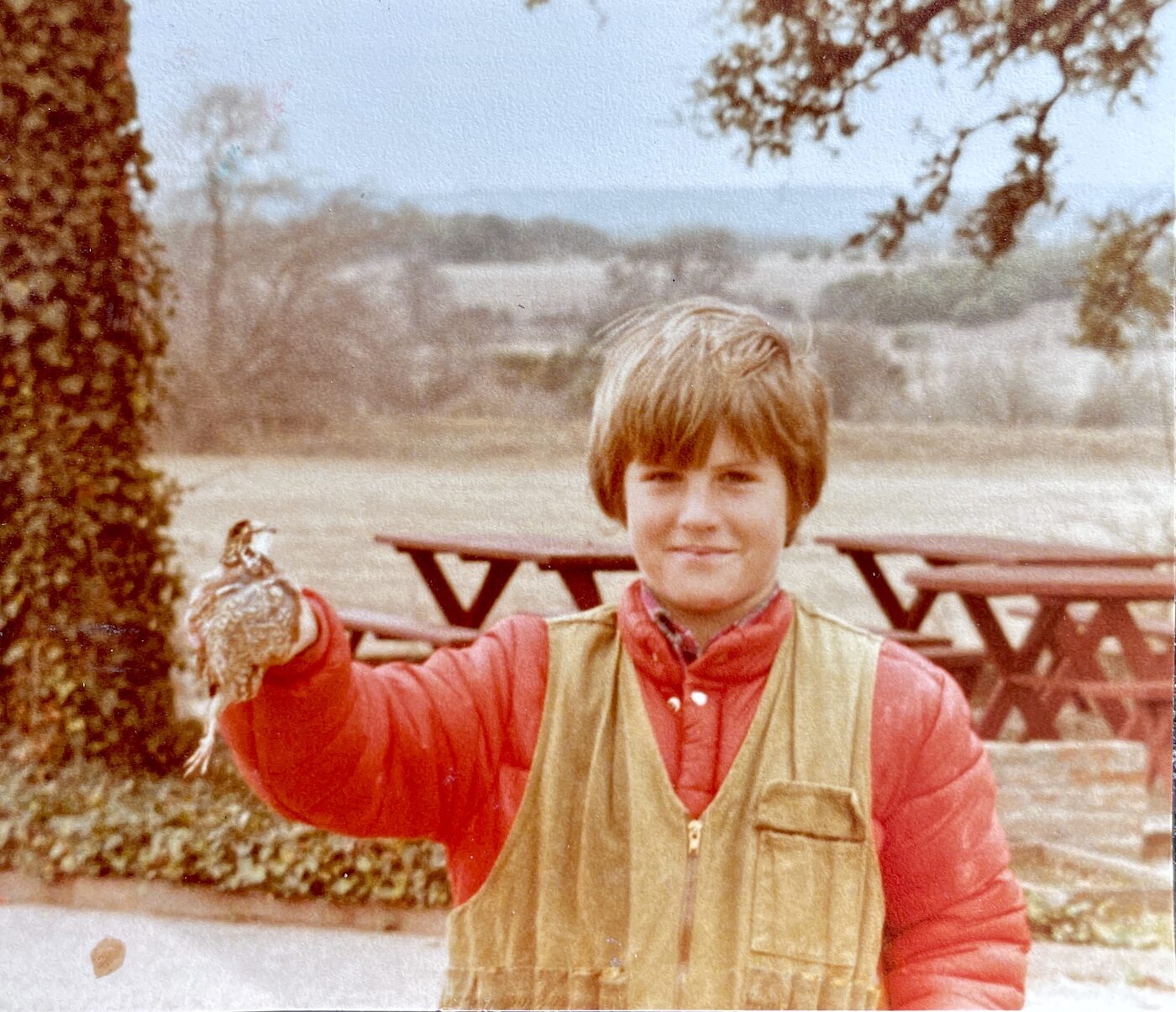 A young Jeb Bradshaw in a red jacket and hunting vest holding up his first bobwhite quail at the Bradshaw farm.