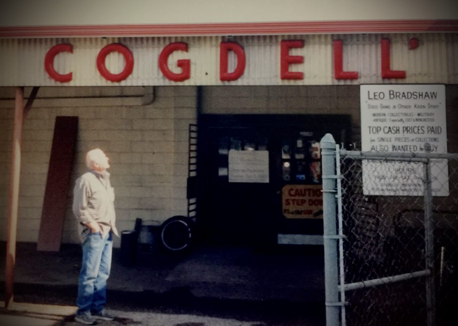 Leo Bradshaw standing outside the Cogdell storefront beneath the large red Cogdell sign.
